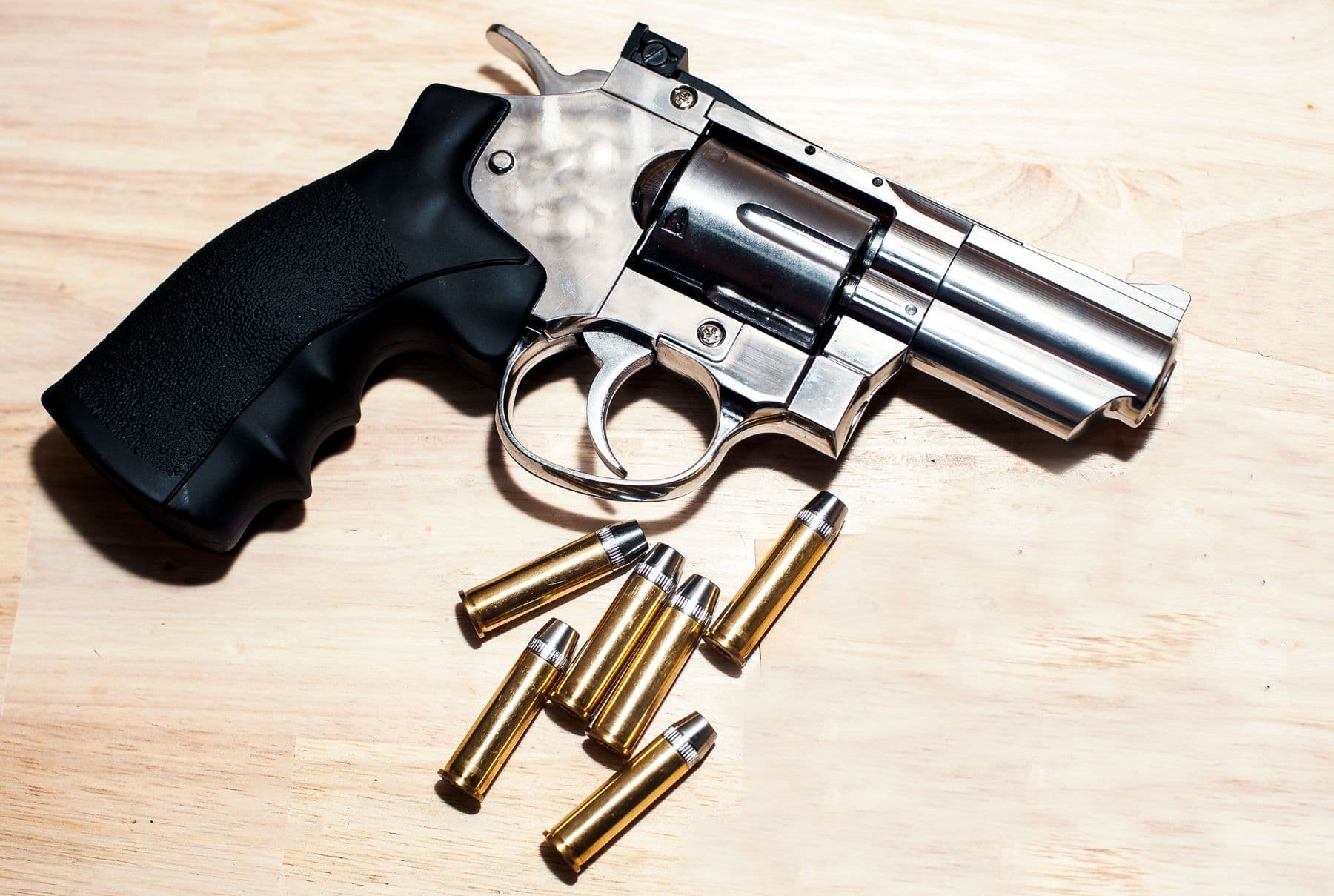 A stainless revolver on a wooden bench with loose cartridges beside it