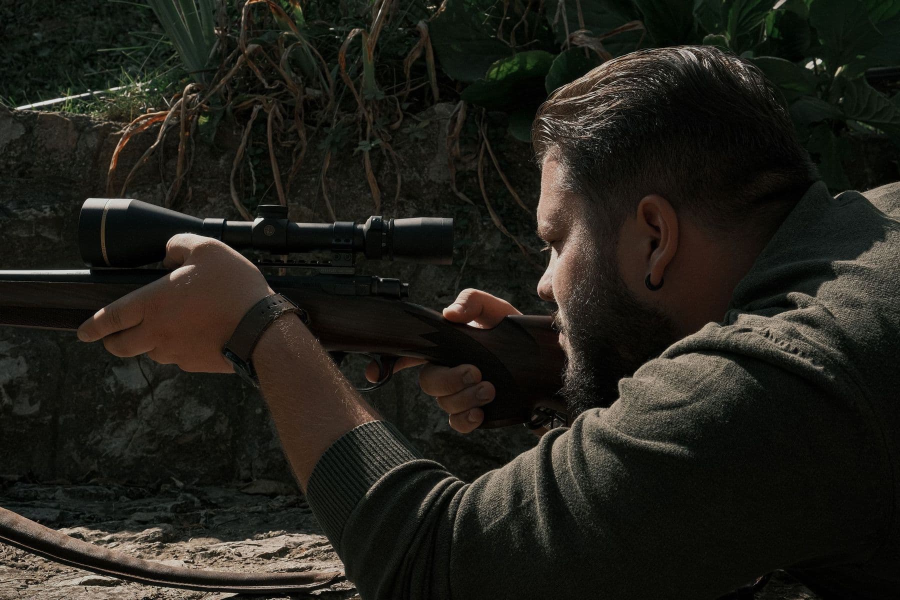A shooter aiming a scoped rifle outdoors